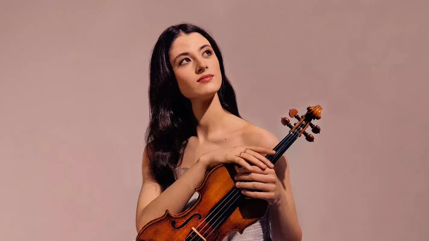 Woman with brown hair looks up into the sky while holding a violin in front of pink background