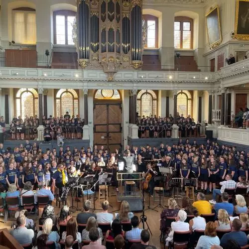 A choir and small orchestra congregate in the auditorium of the Sheldonian Theatre as an audience watches from both the floor and the galleries. 