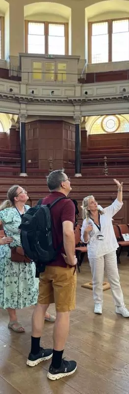 A tour guide gestures to the Sheldonian Theatre ceiling with a small group